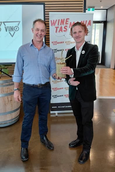 Two men pose smiling in front of a Wine Tasmania banner. 